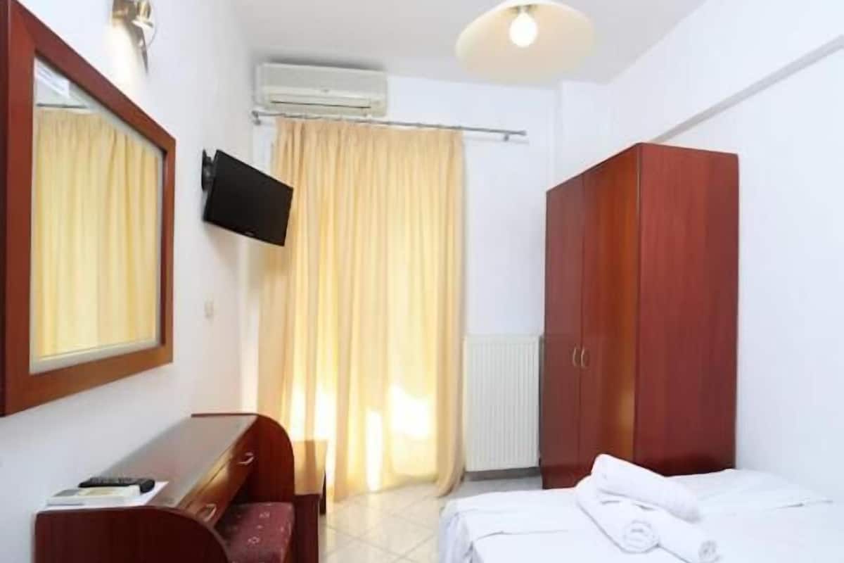 Habitación de hotel con cama, escritorio, silla, armario, televisor y ventana con cortinas.