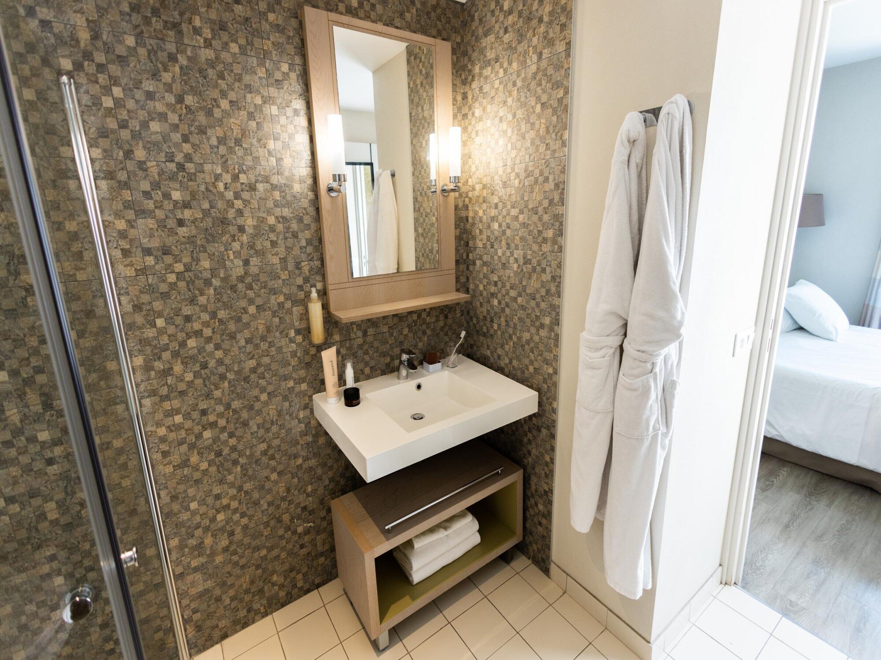 A bathroom with a shower, a sink, a mirror, and a towel rack.