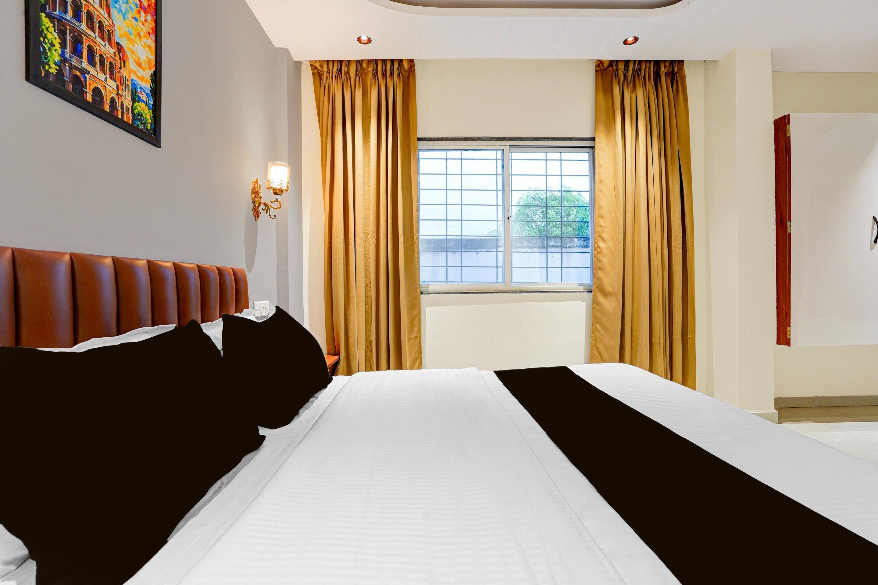 Une chambre d’hôtel avec un grand lit, une tête de lit, une fenêtre avec des rideaux et un luminaire fixé au mur.