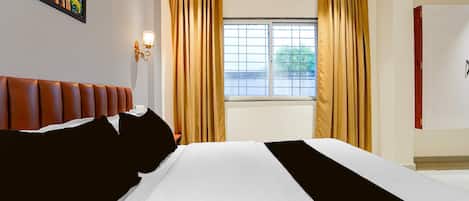 Habitación de hotel con una cama grande, cabecera, ventana con cortinas y una lámpara fijada a la pared.