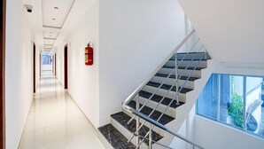 Un interior moderno con una escalera recta, un extintor de incendios sujeto a la pared y una vista despejada al exterior a través de una ventana.