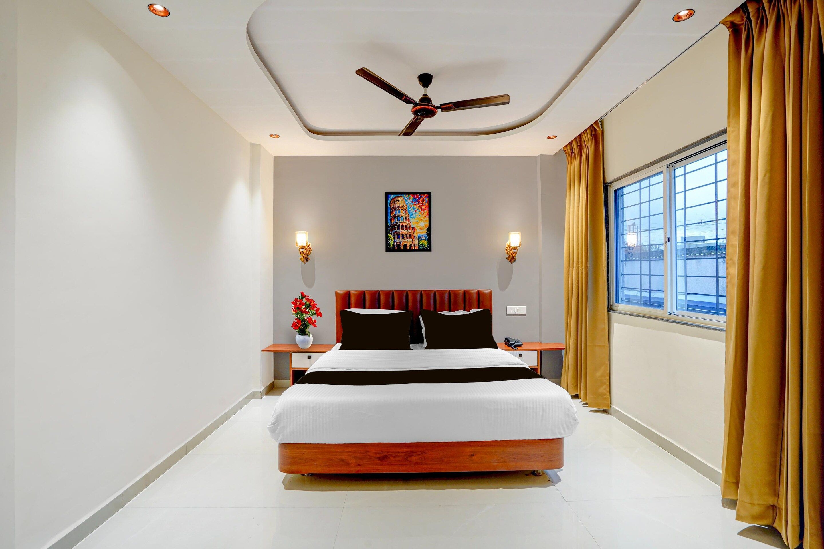 A modern hotel room with a large bed, a ceiling fan, a window with curtains, and a painting on the wall.