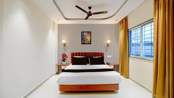 A modern hotel room with a large bed, a ceiling fan, a window with curtains, and a painting on the wall.