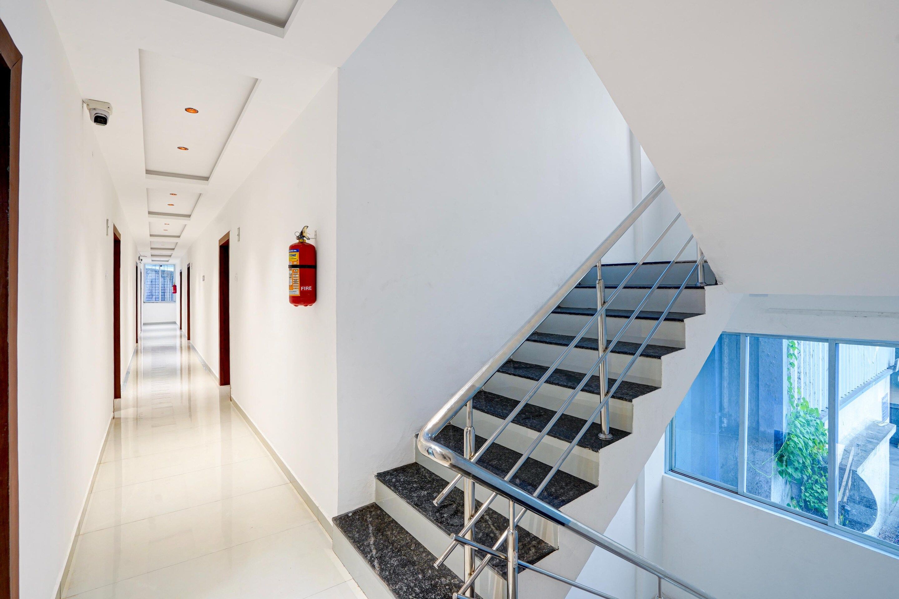 A modern interior with a straight staircase, a fire extinguisher mounted on the wall, and a clear view of the outdoors through a window.