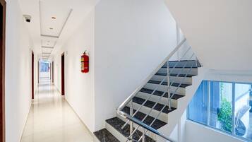 A modern interior with a straight staircase, a fire extinguisher mounted on the wall, and a clear view of the outdoors through a window.