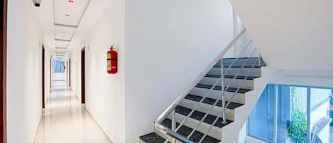 A modern interior with a straight staircase, a fire extinguisher mounted on the wall, and a clear view of the outdoors through a window.