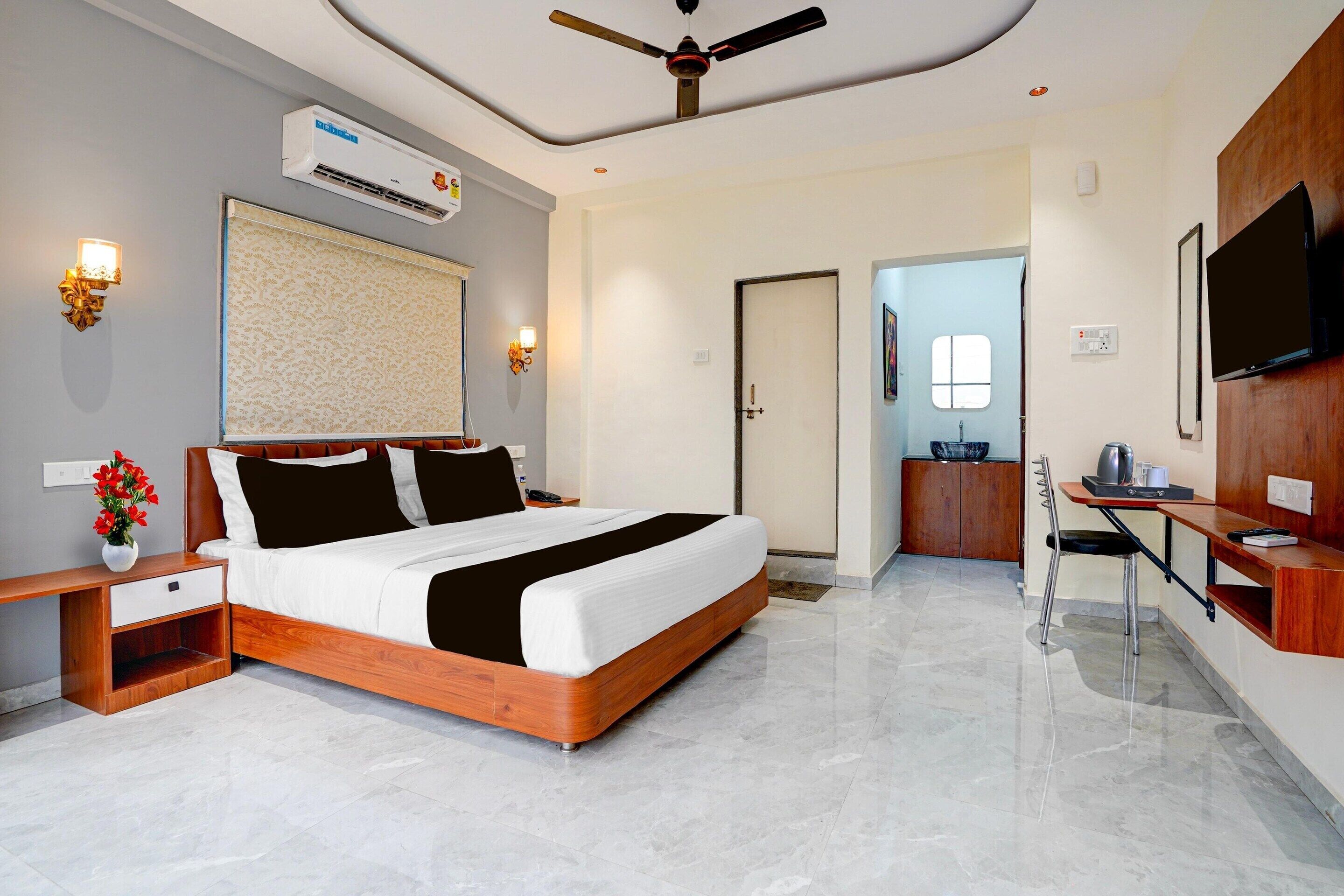 A hotel room with a bed, bedside table, lamp, air conditioning unit, ceiling fan, and a television.