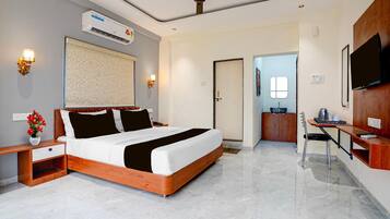 A hotel room with a bed, bedside table, lamp, air conditioning unit, ceiling fan, and a television.