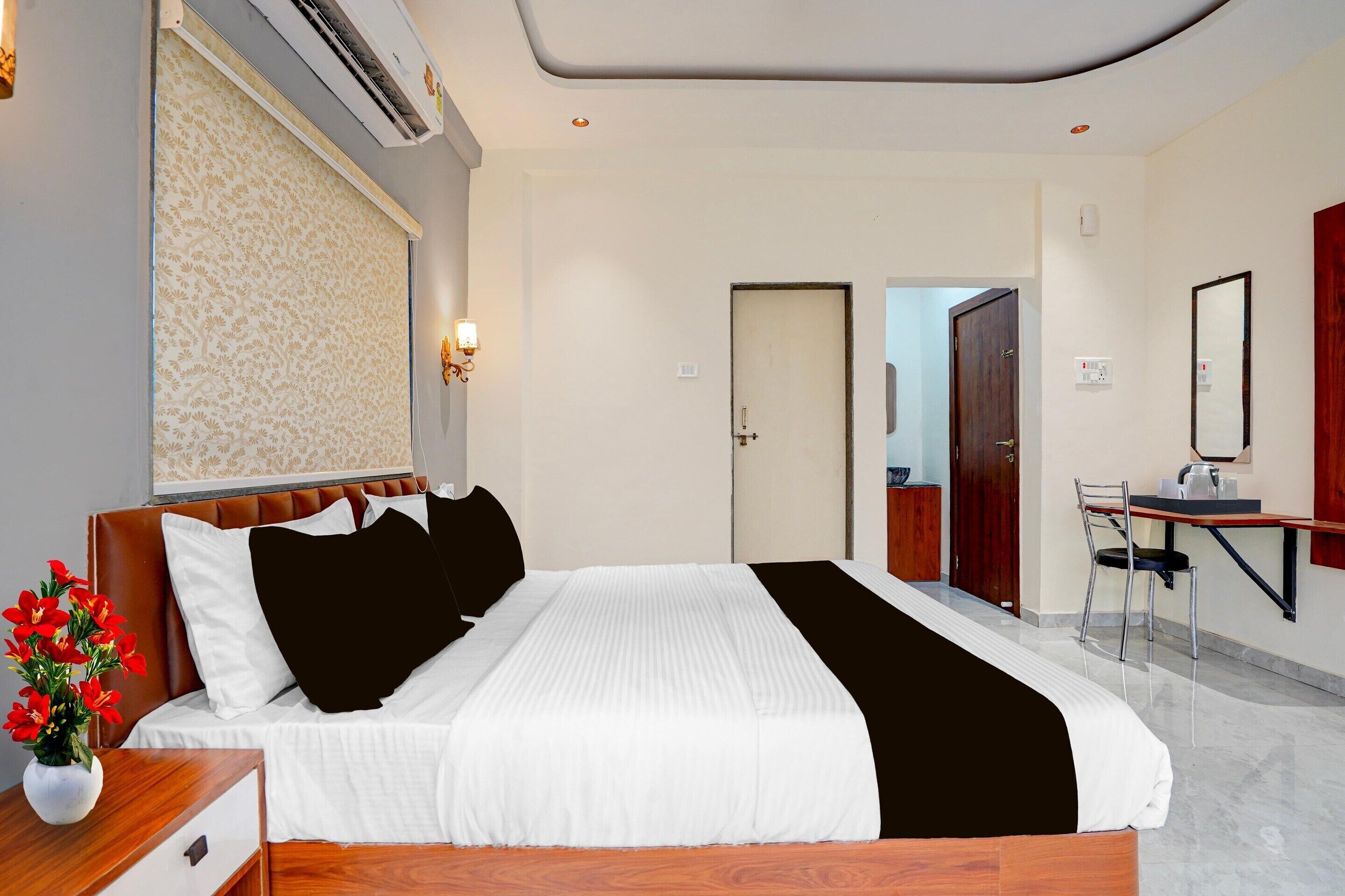 Una habitación de hotel con cama, escritorio, silla, espejo y un florero con flores.