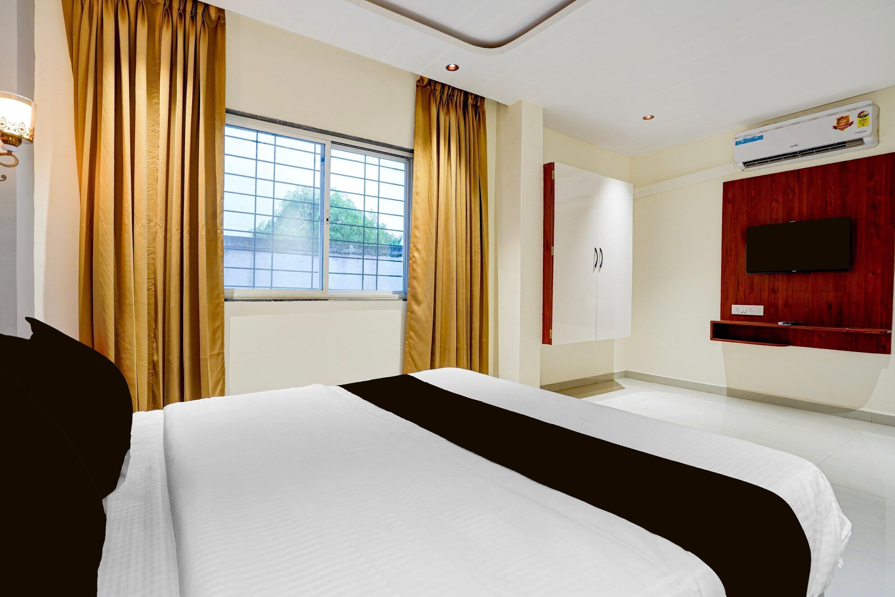 Habitación de hotel con cama, ventana con cortinas, aire acondicionado, televisor montado en la pared y armario.