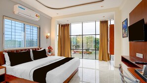 Habitación de hotel con una cama grande, televisión, escritorio y vistas a zonas verdes por las ventanas.