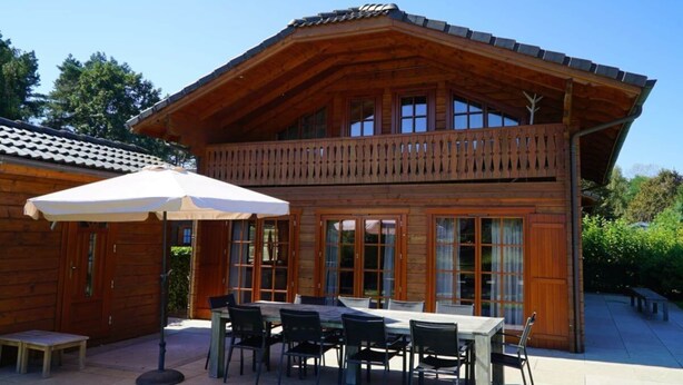 A wooden cabin with a balcony, a dining area with tables and chairs, and a covered patio. - Boekhorst L"etage 10 (Lochem)
