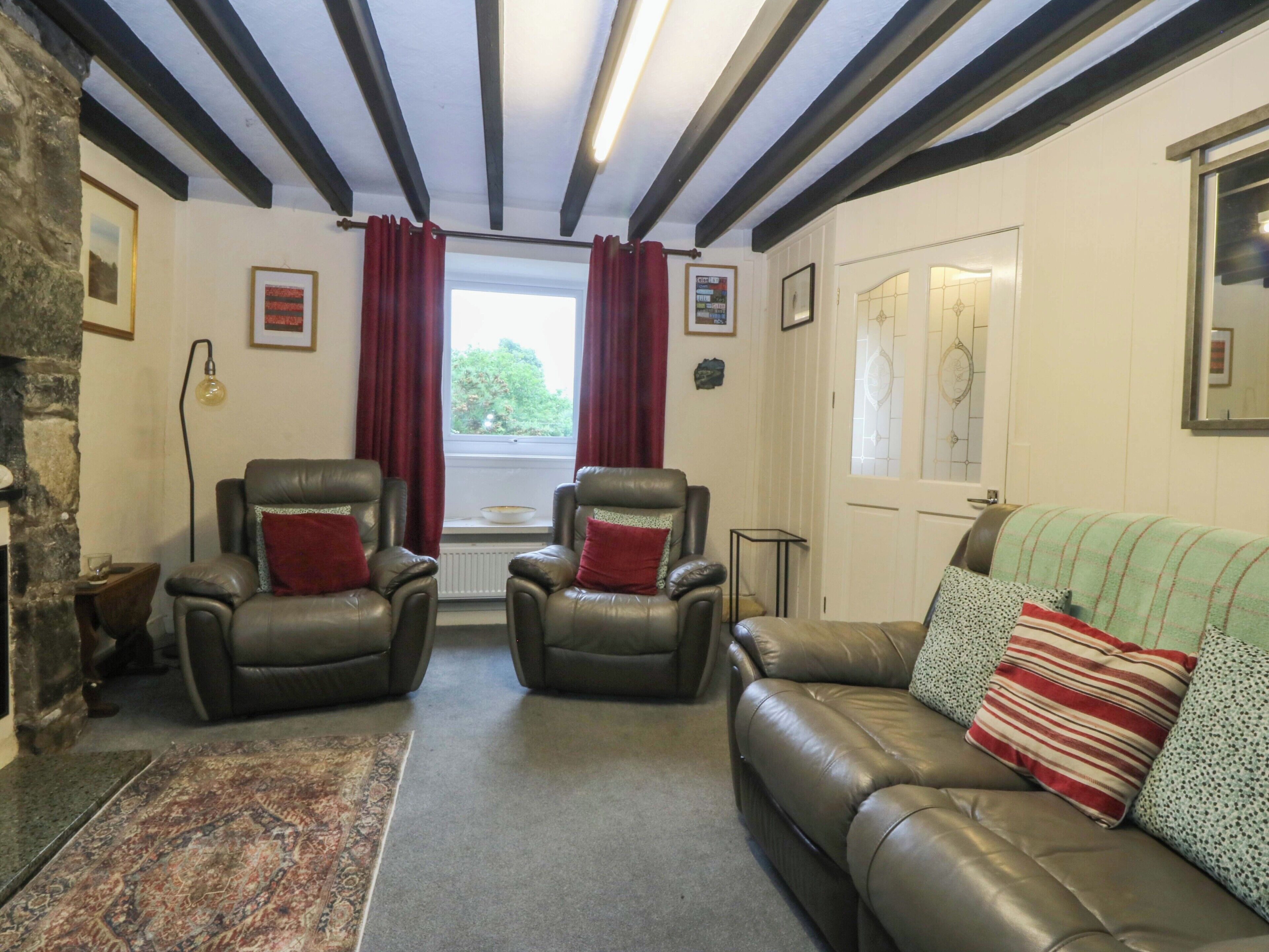 A room with a fireplace, two leather armchairs, a sofa, a rug, and a window with curtains.