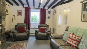 A room with a fireplace, two leather armchairs, a sofa, a rug, and a window with curtains.