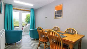 Uma sala de jantar com uma mesa e cadeiras de madeira, poltronas cor verde-água e vista através de uma porta de vidro.