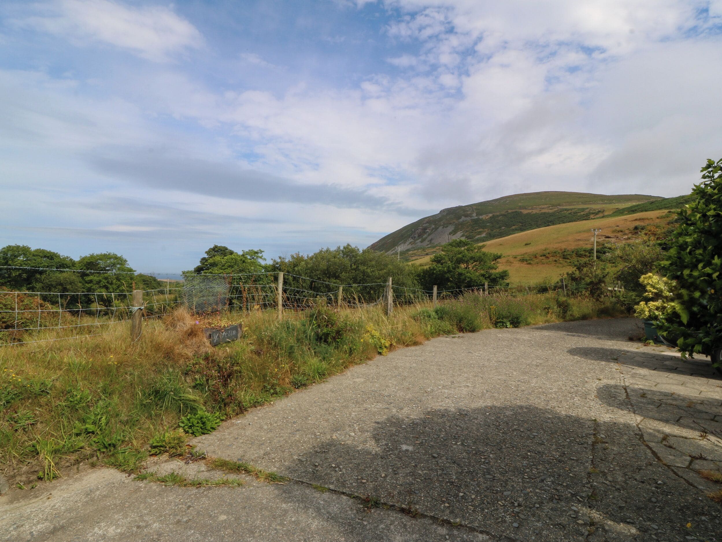 A rural road with a metal fence and a signpost, surrounded by greenery and hills.