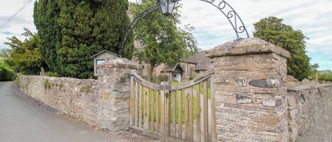 A stone gate with a wooden fence, a lamp post, and a tall tree in the background.