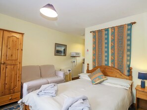 A hotel room with a bed, a wooden wardrobe, a sofa, a bedside table with a lamp, and a wall-mounted air conditioner. - Apartment 3 (Lydbury North)
