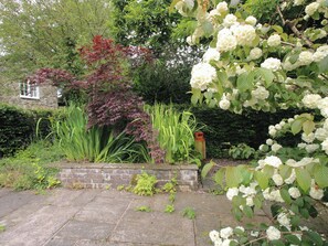 A garden with a variety of plants, a brick wall, and a stone pathway. - Apartment 3 (Lydbury North)