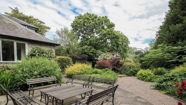 Eine Garten-Terrasse mit Tisch und Bänken, umgeben von verschiedenen Pflanzen und Bäumen.