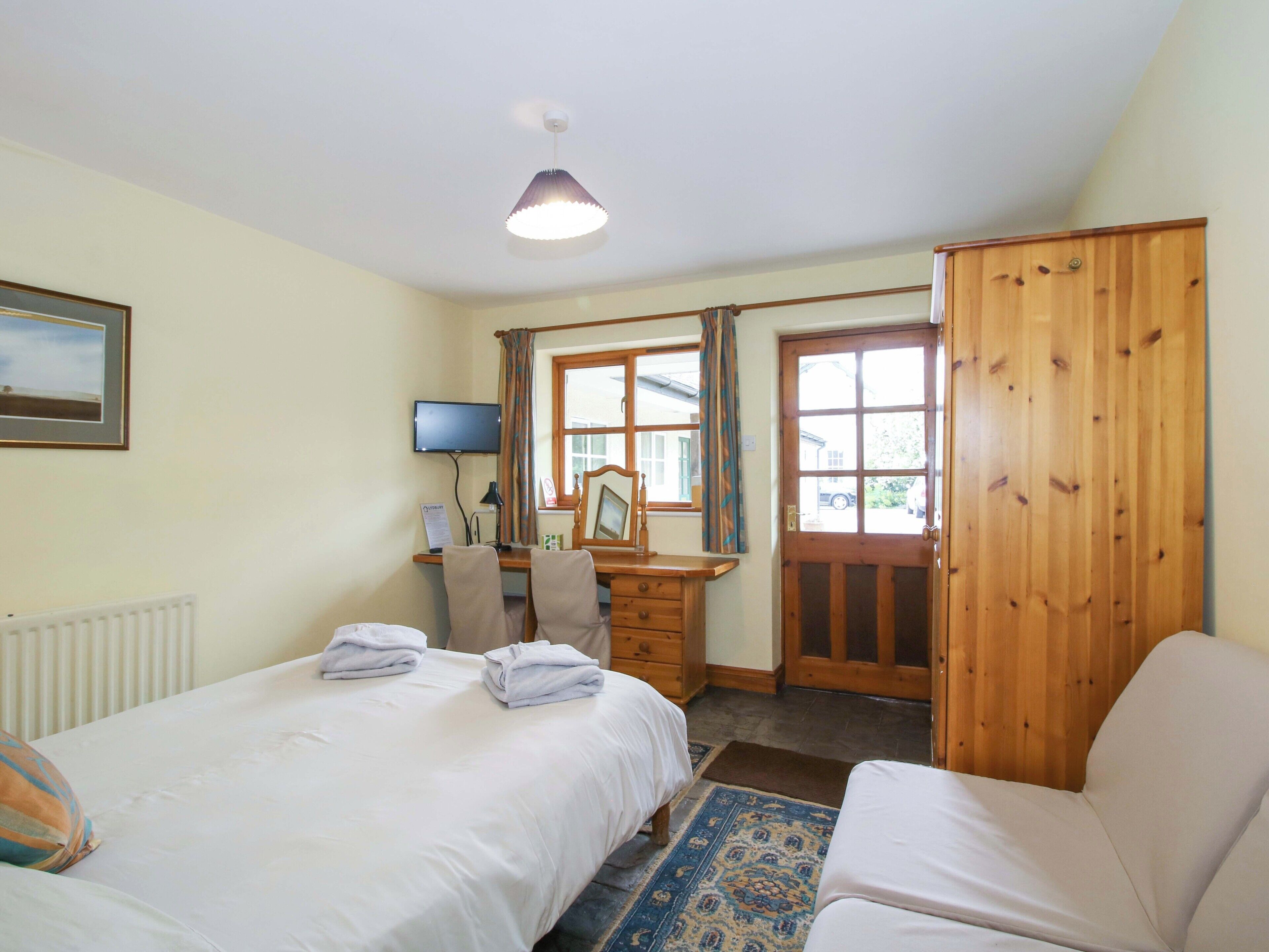 A bedroom with a bed, a desk, a chair, a wardrobe, and a television.