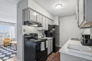 A modern kitchen with white cabinets, a black stove, and a refrigerator. - Wilcrest Apartments by Andes STR (Houston)