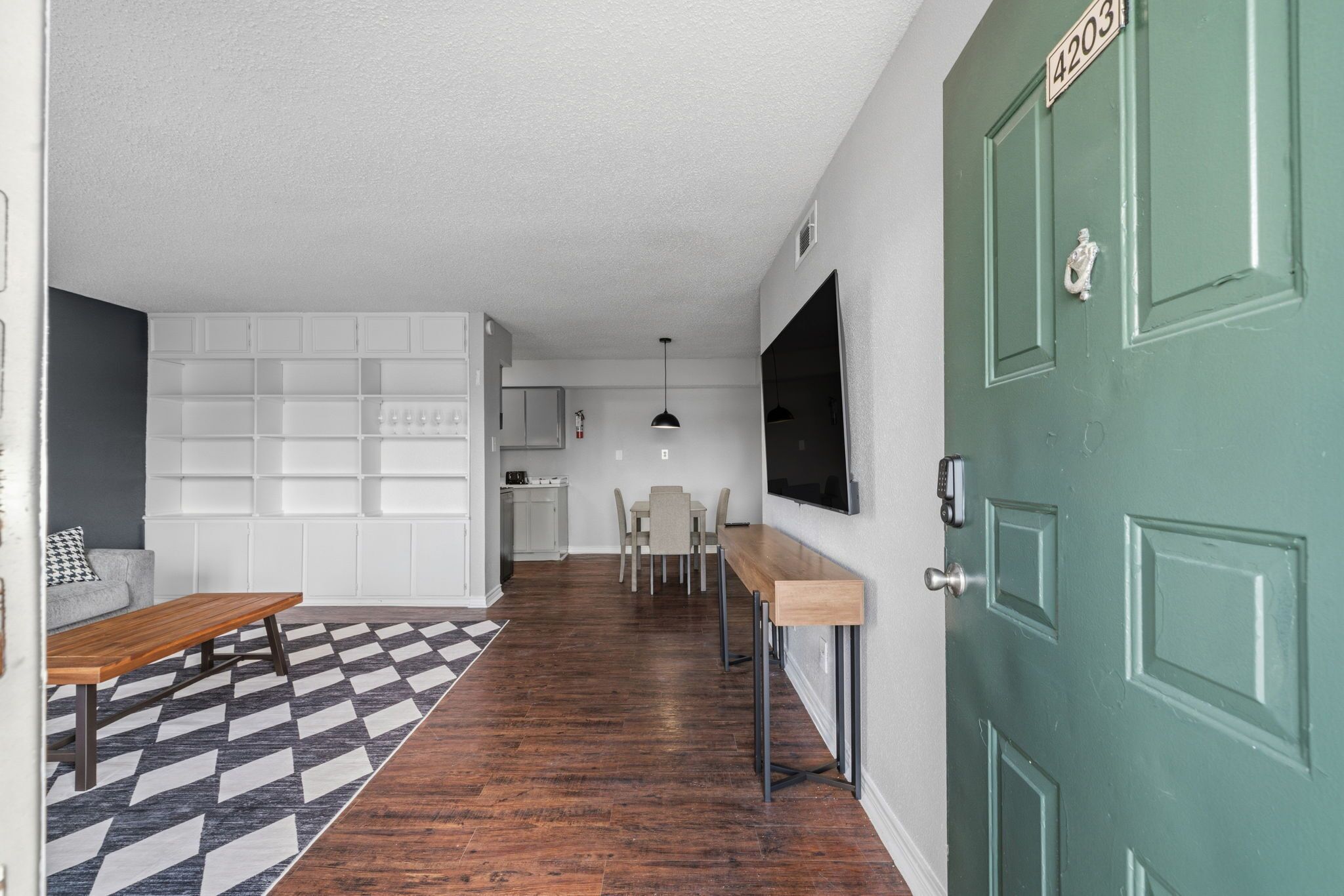 A modern interior with a dining area, kitchen, and a green door.