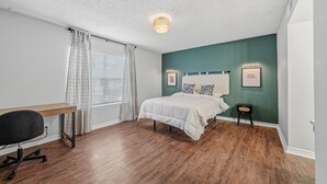A bedroom with a bed, a desk, and a chair. - Wilcrest Apartments by Andes STR (Houston)