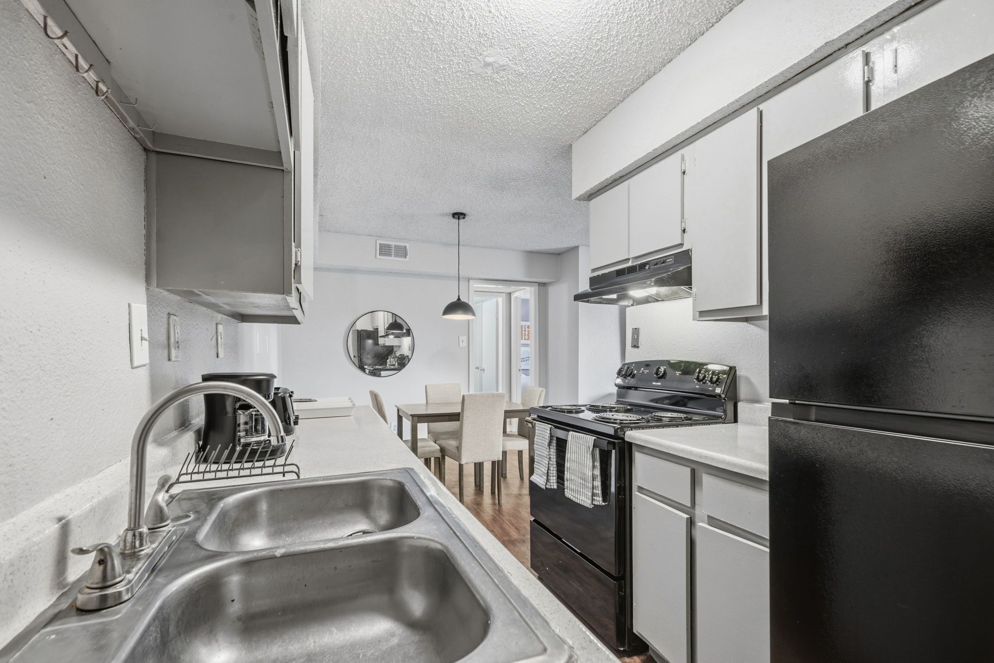 A modern kitchen with stainless steel appliances, a double sink, and a dining area with chairs.