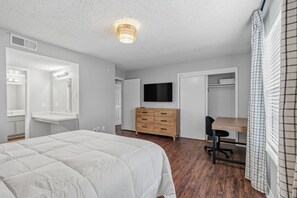 A bedroom with a bed, dresser, TV, and a desk with a chair. - Wilcrest Apartments by Andes STR (Houston)