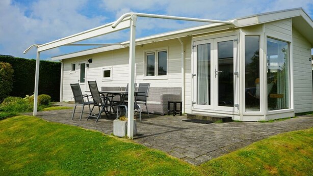 A single-story house with a covered patio, a dining area with chairs, and a glass door entrance. - Holiday Home in Breskens With Terrace (Breskens)