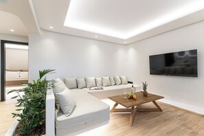 A modern living room with a sectional sofa, a coffee table with fruits, and a flat-screen TV mounted on the wall. - Naxian Spirit Luxury Villas Plaka (Plaka)
