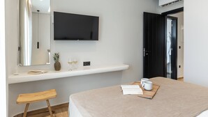 Moderni hotellihuone, jossa on seinälle asennettu taulutelevisio, pieni puujakkara, beigenvärinen vuode ja minibaari.