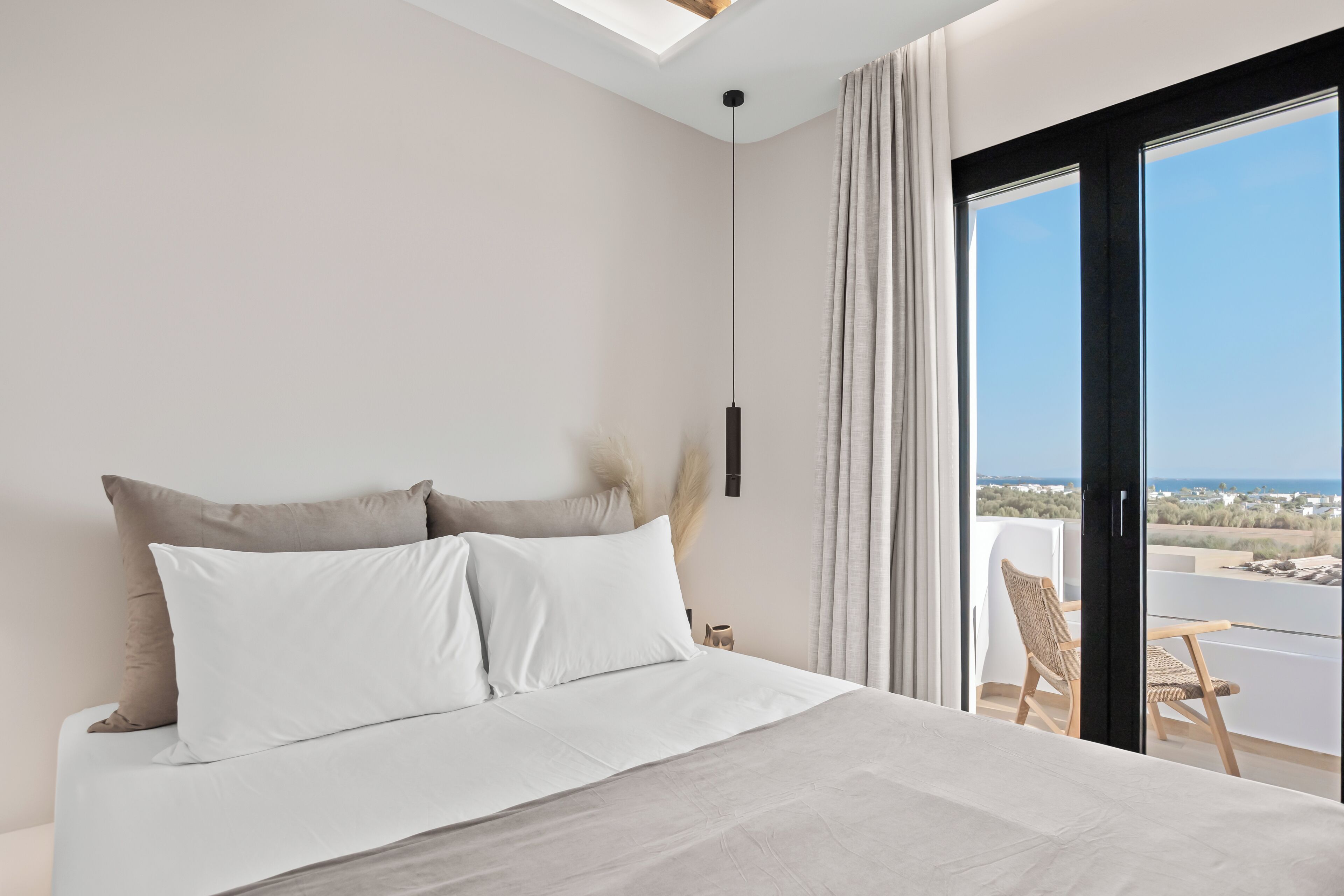 A bedroom with a large bed, a view of the sea, and a balcony with chairs.