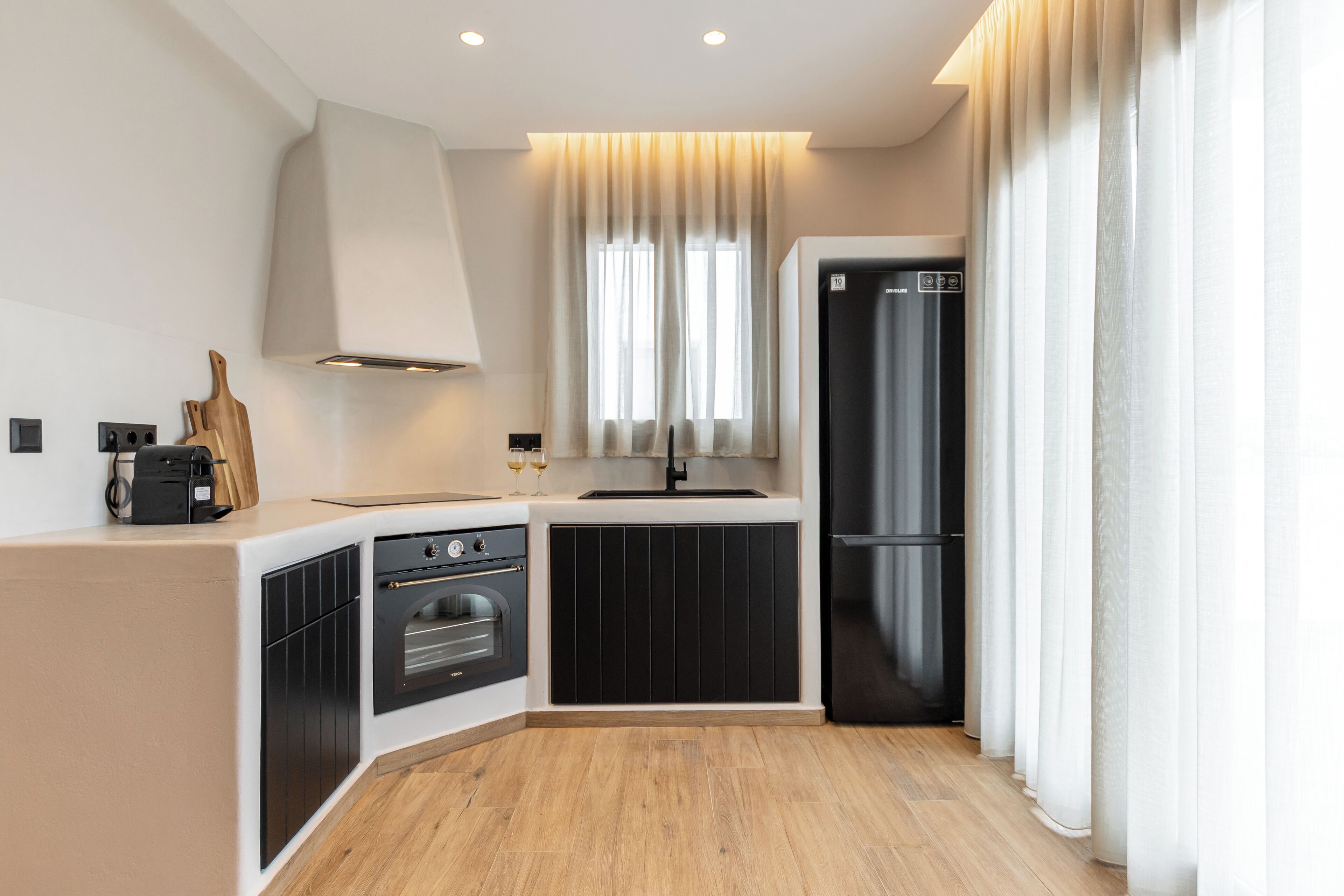 A modern kitchen with a built-in oven, a refrigerator, and a window with curtains.
