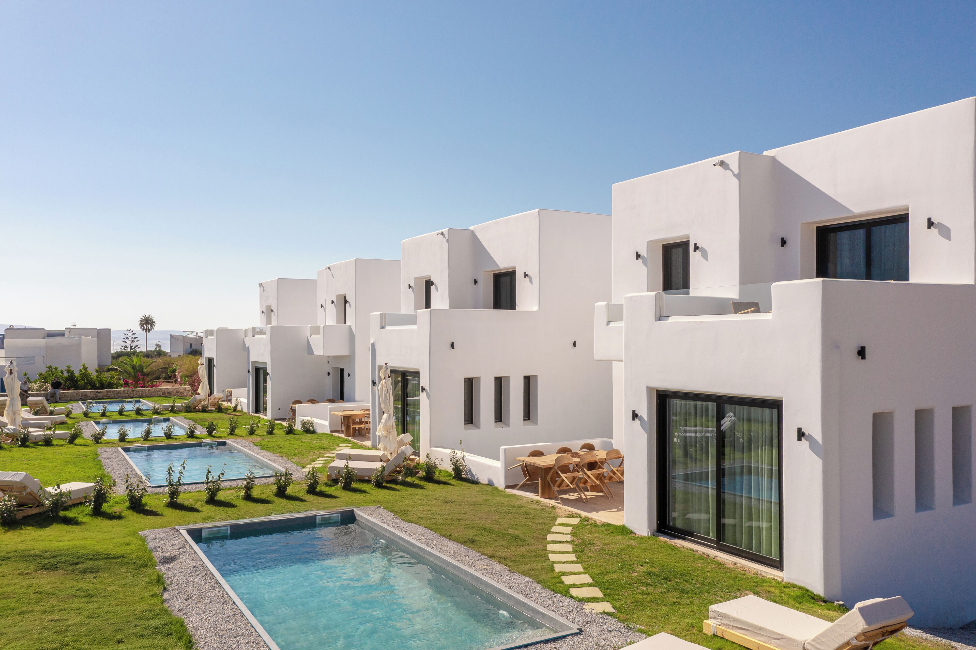 Un moderno resort con varias edificaciones blancas, una piscina y zonas de estar al aire libre.