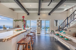 Cocina moderna con barra, taburetes de madera y vista al océano.