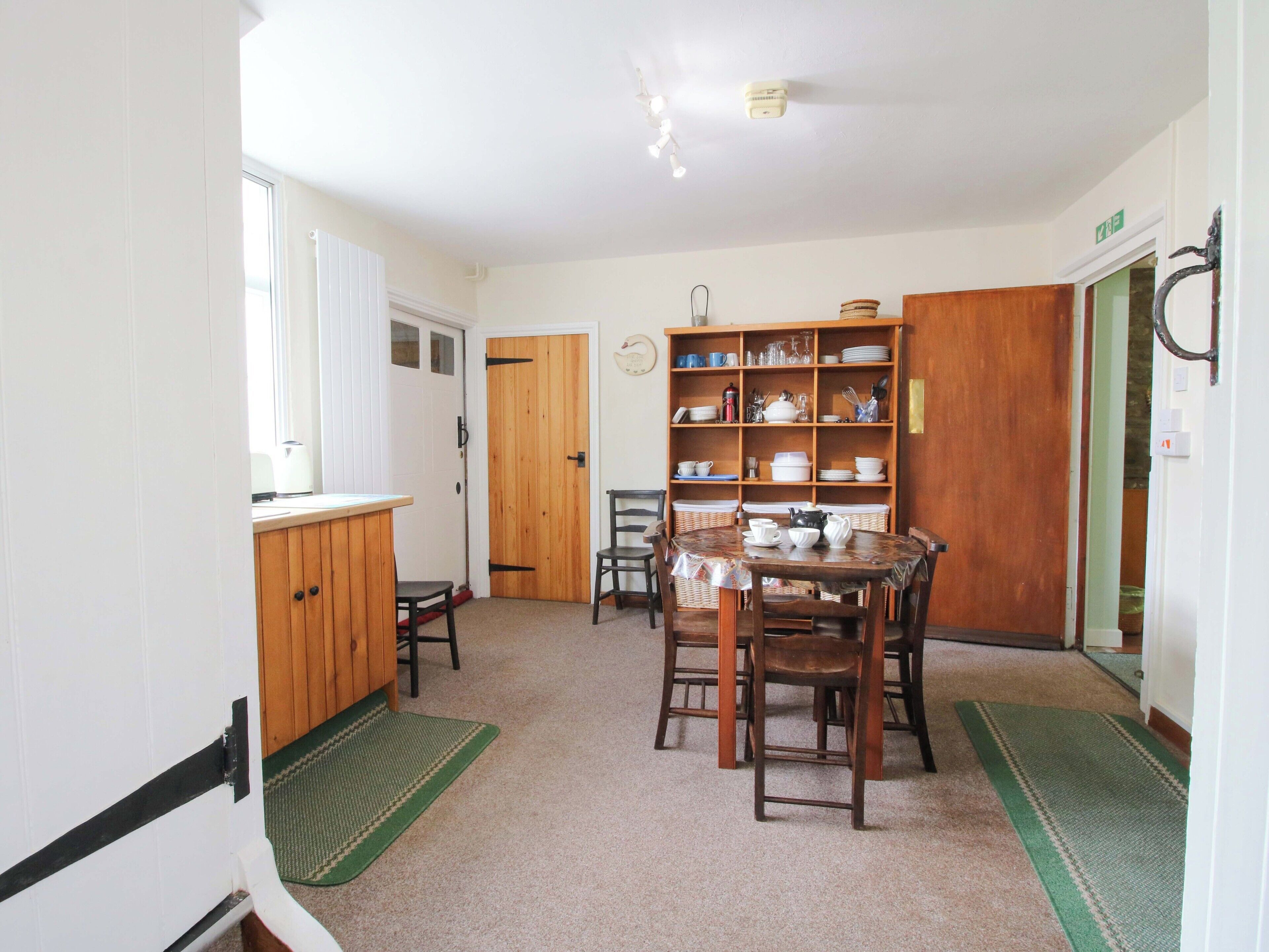 A kitchen with a dining table, chairs, a wooden cabinet, and a shelf with dishes.