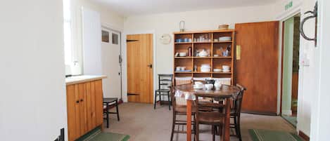 A kitchen with a dining table, chairs, a wooden cabinet, and a shelf with dishes.