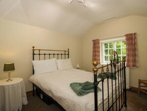 A bedroom with a bed, a bedside table, a lamp, a window with curtains, and a chair. - Kwerky Cottage (Lydbury North)