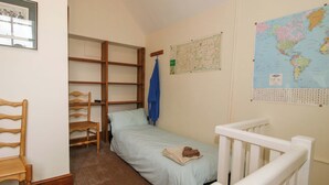Een kleine eenpersoonskamer met een houten stoel, een kaart en een lijst aan de muur.