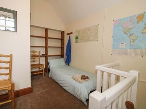 Ein kleines Zimmer mit einem Einzelbett, einem Holzhocker, einer Karte und einem gerahmten Bild an der Wand.