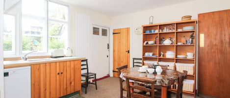 Una cocina con gabinetes de madera, un lavamanos, una mesa de comedor con sillas y una estantería empotrada con vajilla.