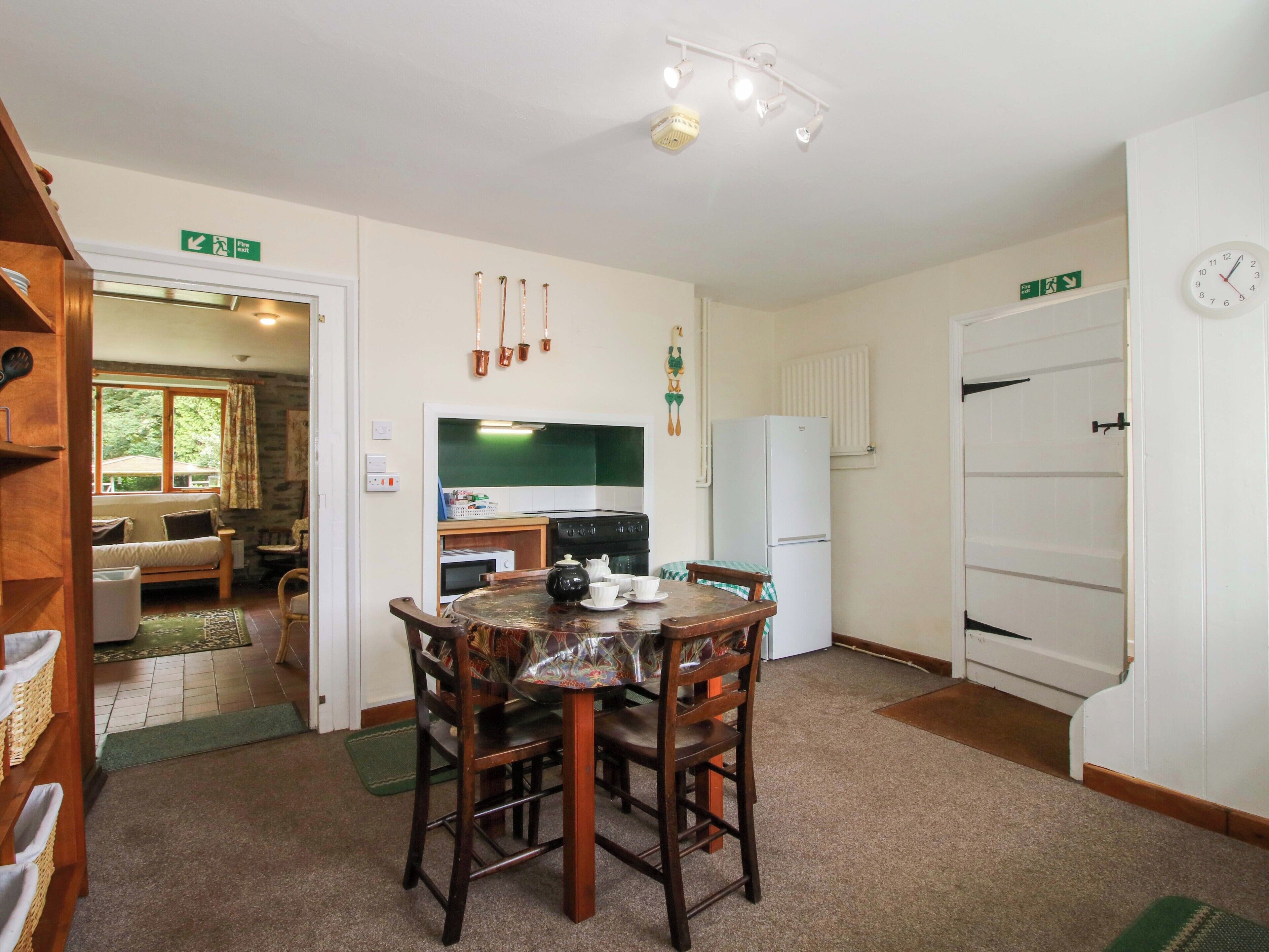 A compact kitchen with a dining table, chairs, a refrigerator, and a clock on the wall.