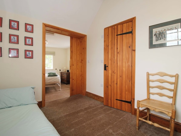 A bedroom with a bed, a wooden door, a chair, and a wall with framed pictures. - Kwerky Cottage (Lydbury North)