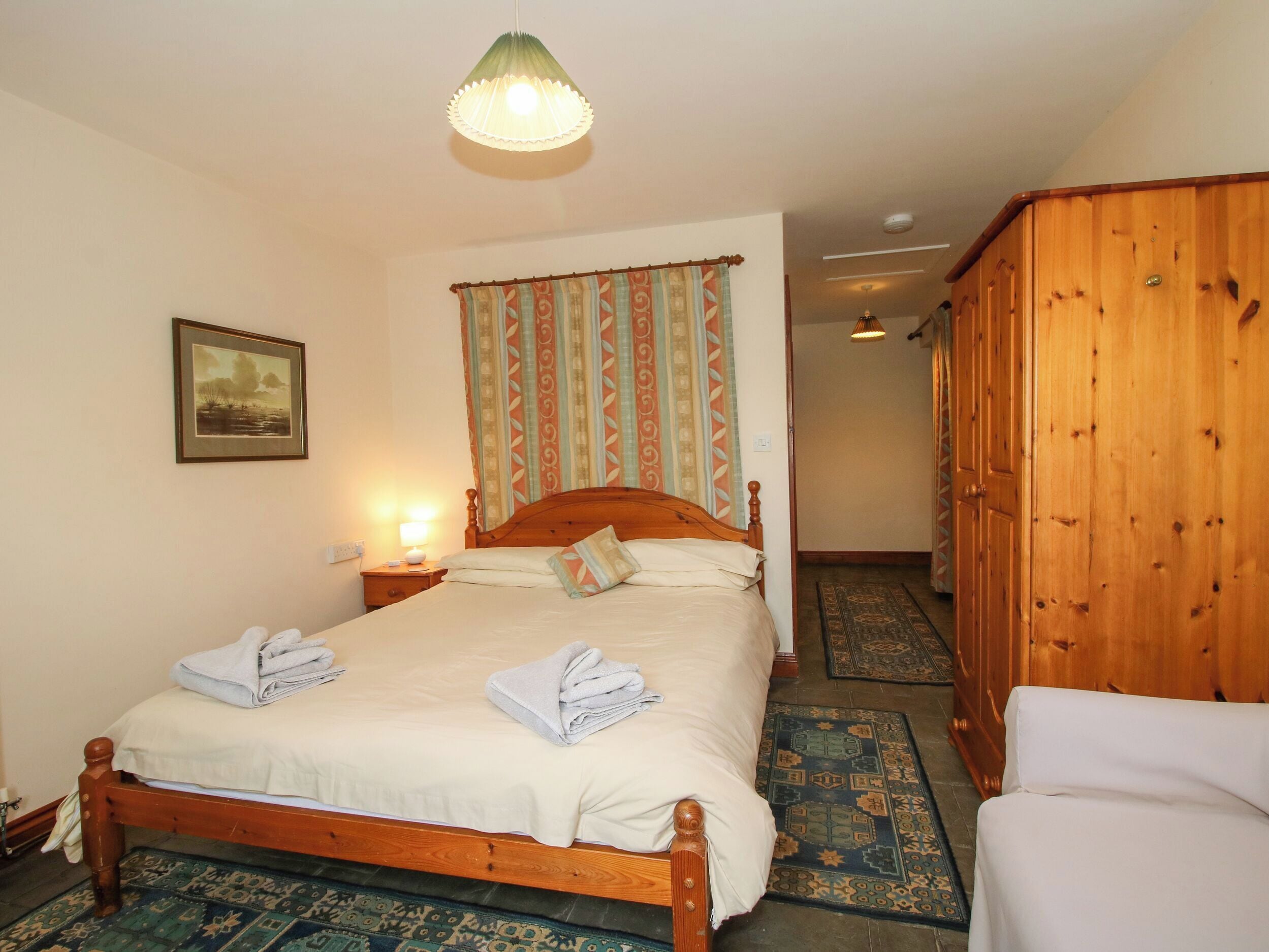 A bedroom with a wooden bed, a nightstand with a lamp, a wardrobe, and a patterned carpet.