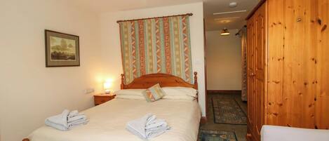 A bedroom with a wooden bed, a nightstand with a lamp, a wardrobe, and a patterned carpet.
