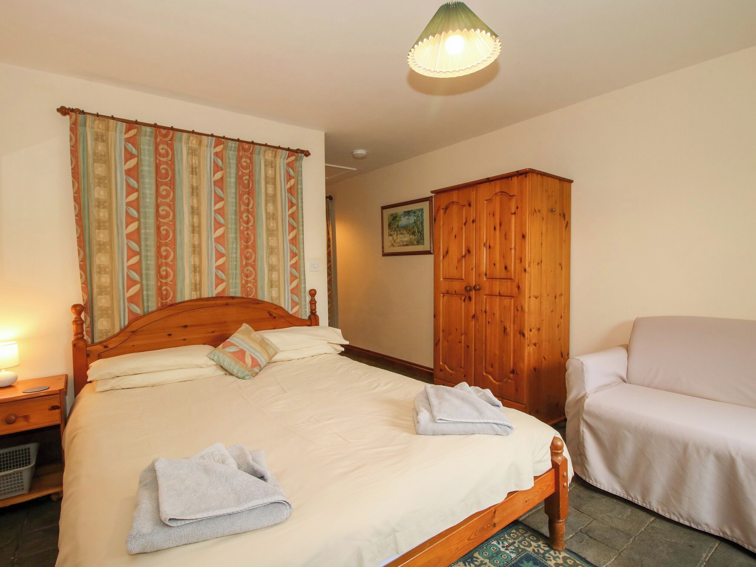 A bedroom with a wooden bed, a wardrobe, a chair, and a lamp.