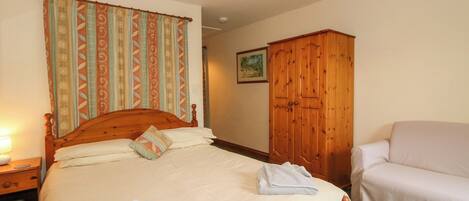 A bedroom with a wooden bed, a wardrobe, a chair, and a lamp.