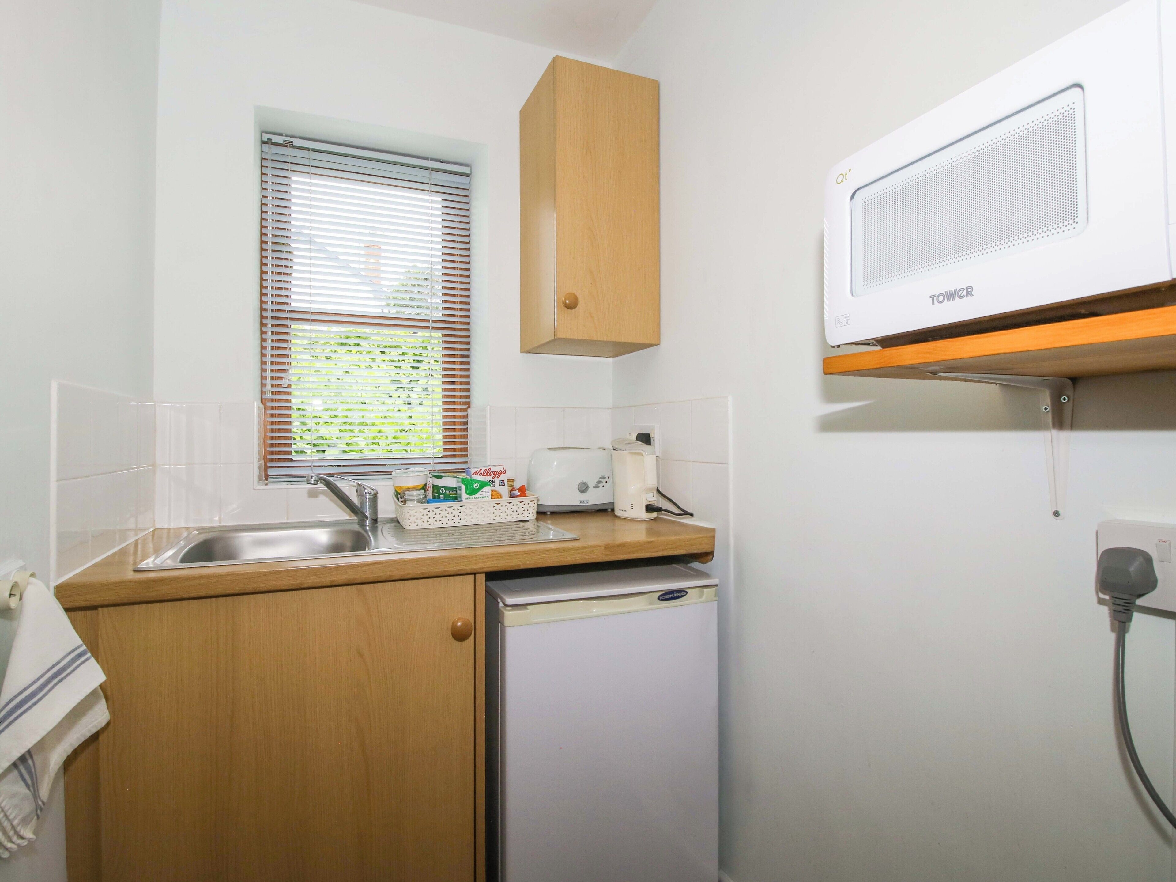 Eine kleine Küche mit Spüle, Toaster, Kühlschrank und einem Fenster mit Jalousien.